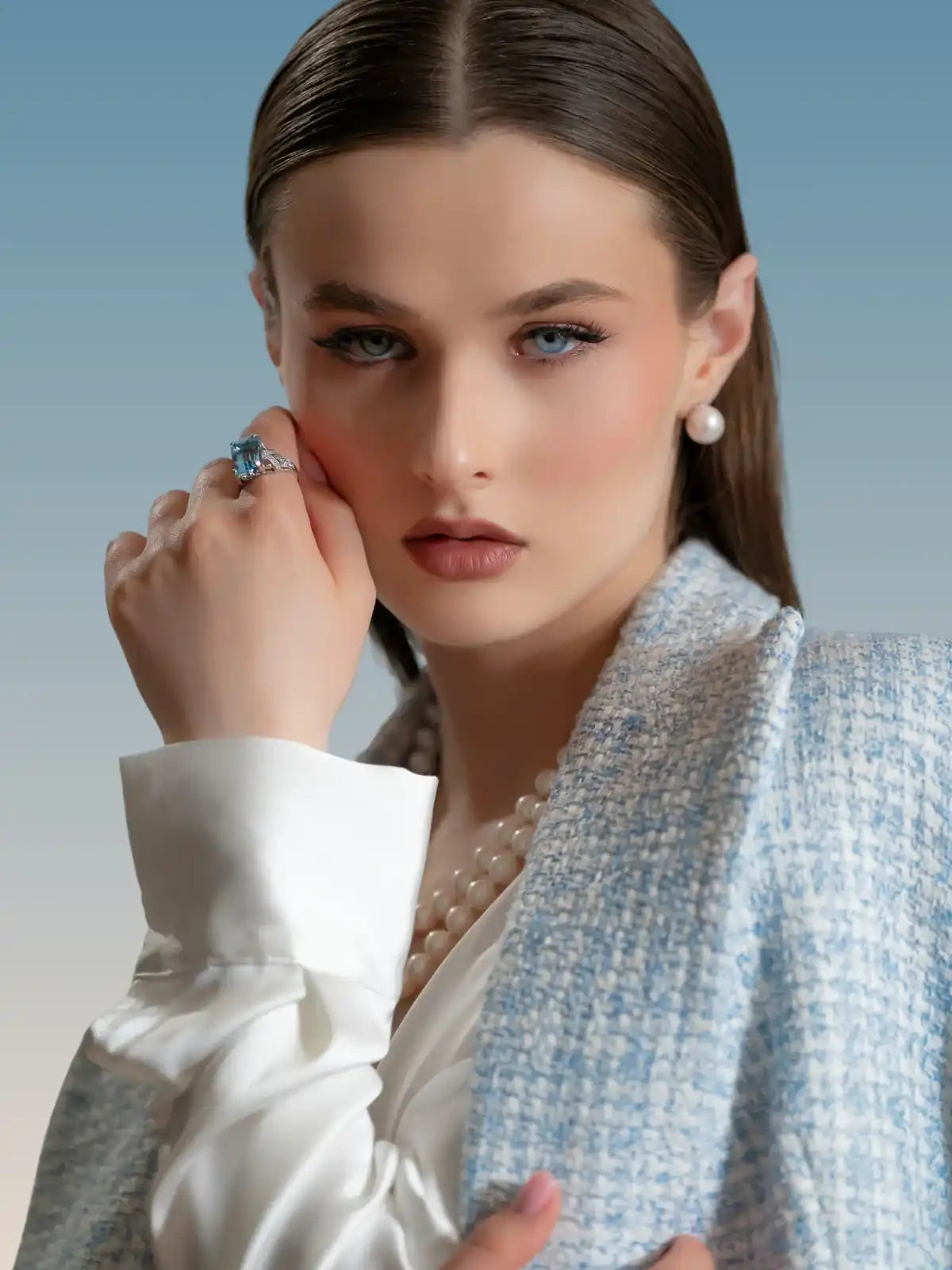 Close-up of woman wearing pearl earrings, pearl necklace, blue gemstone ring, and blue textured jacket
