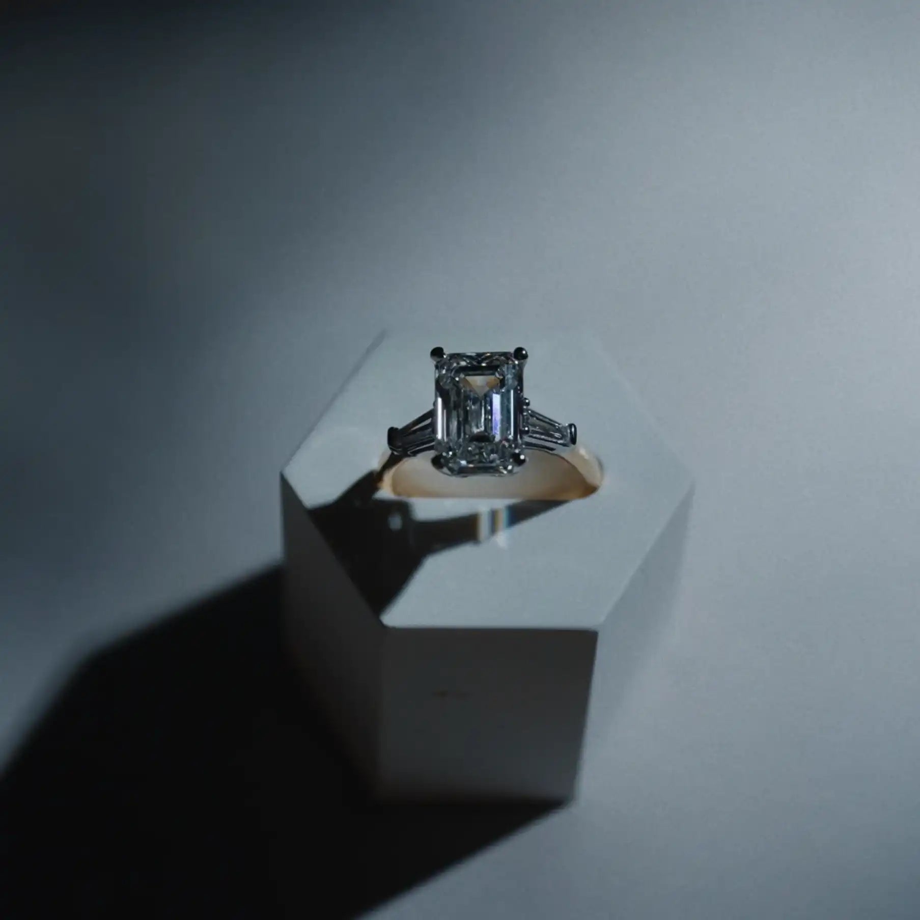 Elegant emerald cut diamond engagement ring on geometric white display, fine jewelry by VELA Jewellers